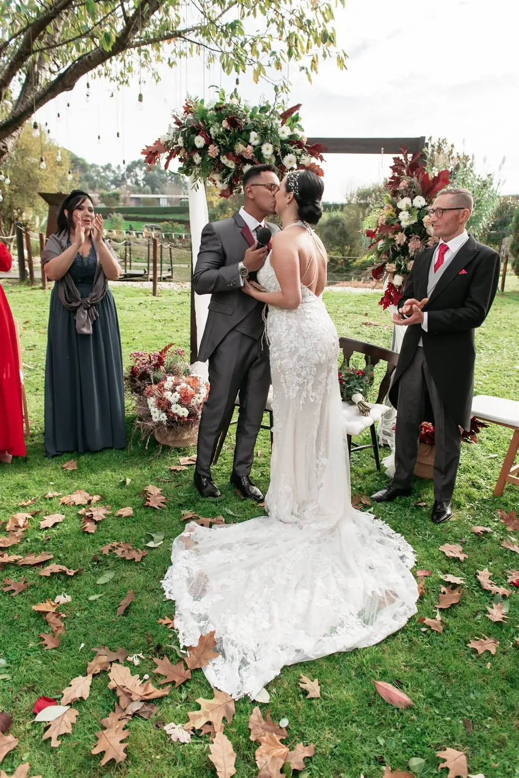 The couple’s kiss beneath a floral arch at an outdoor autumn ceremony