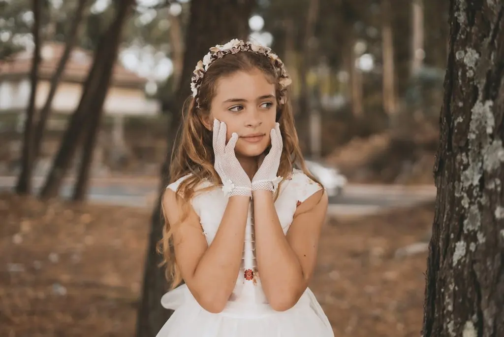 A girl in a flower crown and white gloves rests her hands on her cheeks