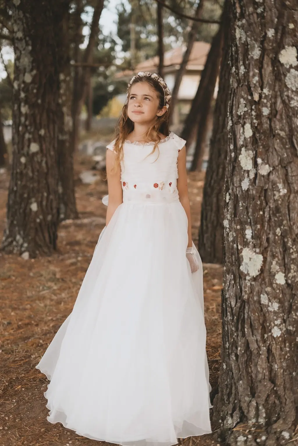 A girl in a white dress embroidered with flowers among pine trees