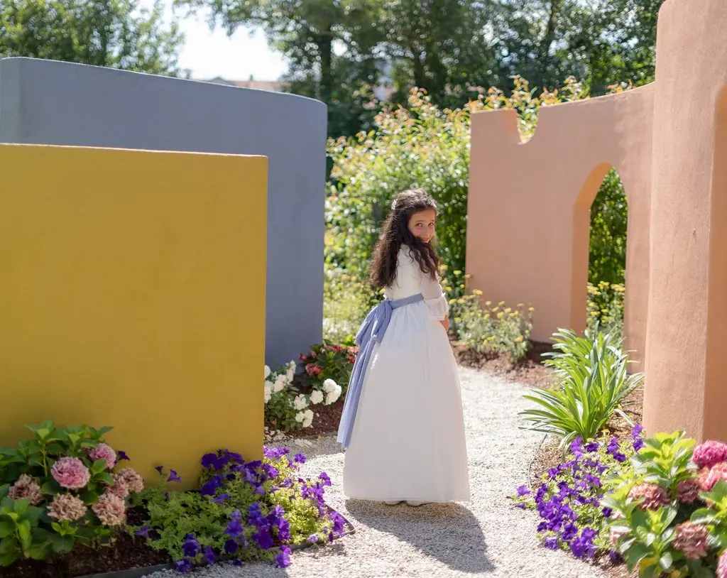 A girl dressed in white at the far end of a garden of colorful walls and flowers