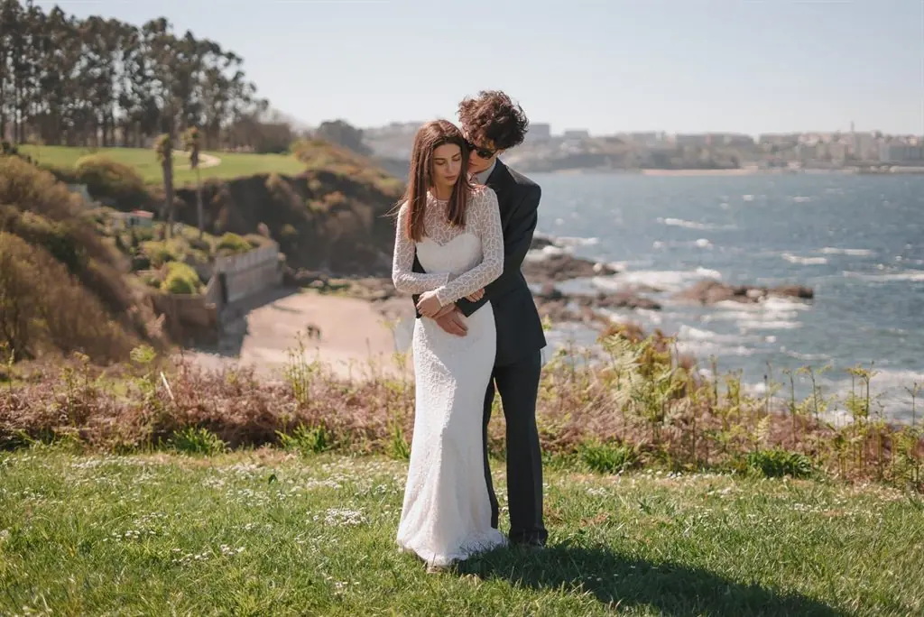 A couple in wedding attire embracing on a seaside cliff in daylight