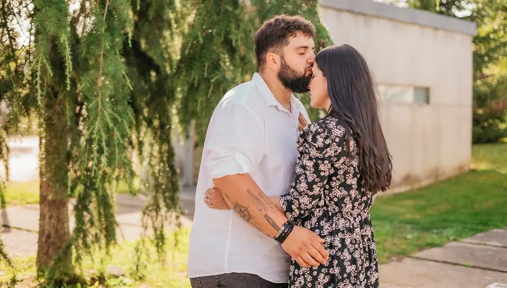 A couple embrace and he kisses her forehead beneath a weeping tree