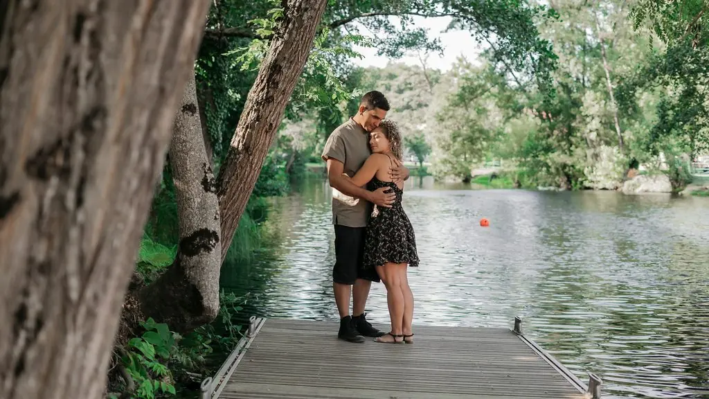 A couple embrace on a wooden jetty beside a calm river, among trees