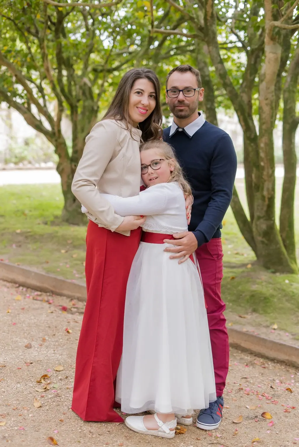 A mother and father embrace their daughter beneath trees
