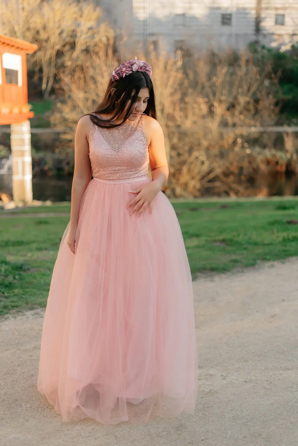 A young woman in a long pink tulle dress and a flower crown in a park at sunset