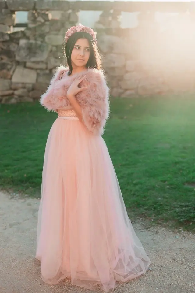 Una joven con falda de tul rosa y bolero de plumas, a contraluz junto a un muro de piedra