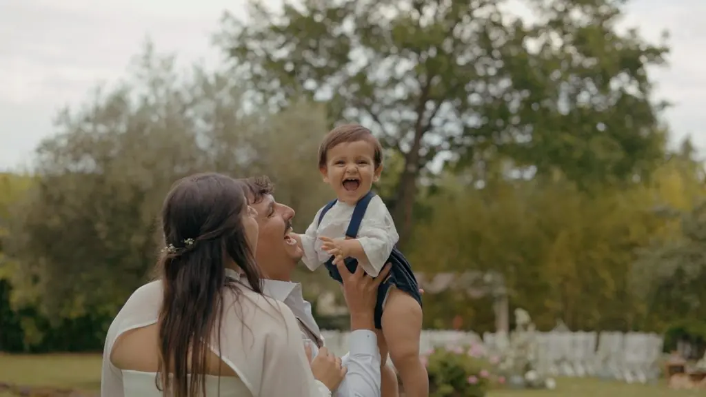 A woman holds a smiling child in her arms, trees behind them