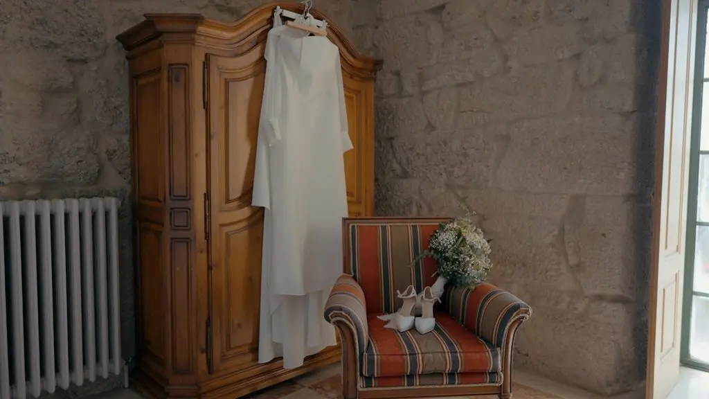 The wedding dress hanging on an antique wardrobe, the bouquet on an armchair