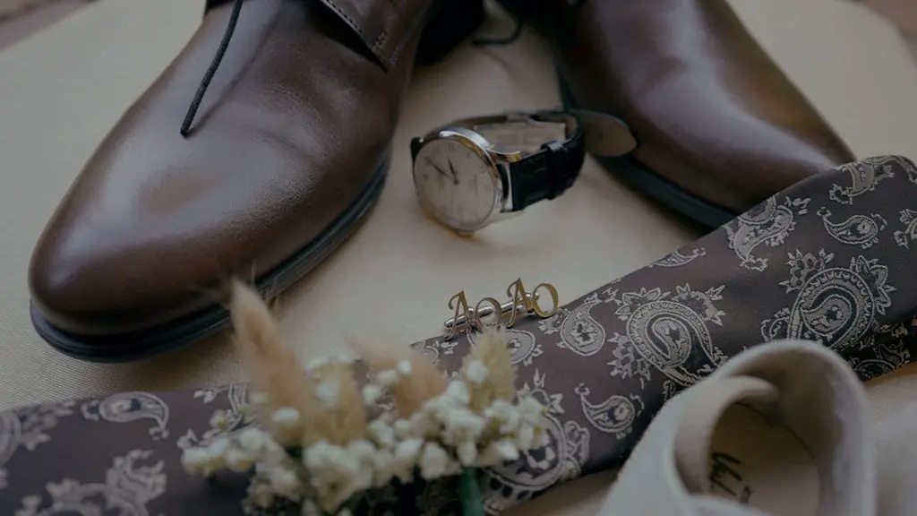The groom’s shoes, watch, tie and a dried flower laid out on a table