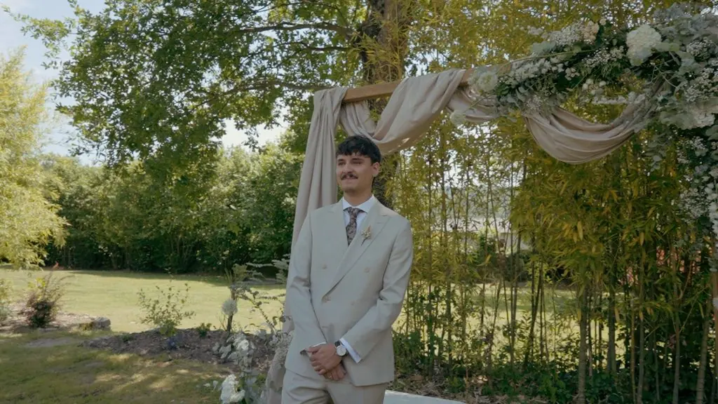 The groom waits beneath a draped floral arch in the garden