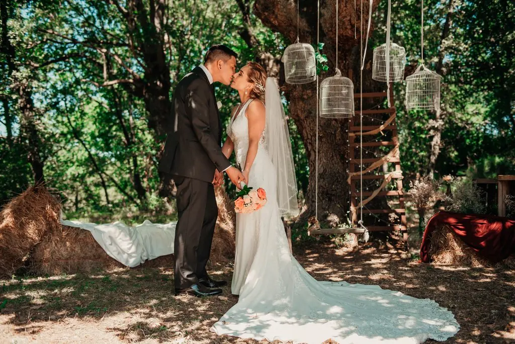 The couple kiss beneath a tree hung with decorative cages, the veil trailing on the ground